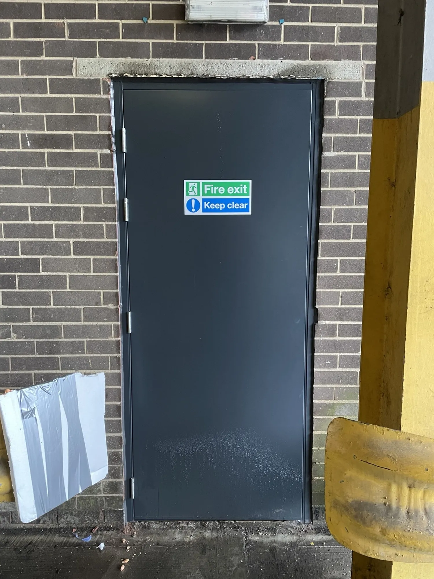 New steel exit doorset fitted in its place, closed, with 'Fire exit / Keep clear' signage