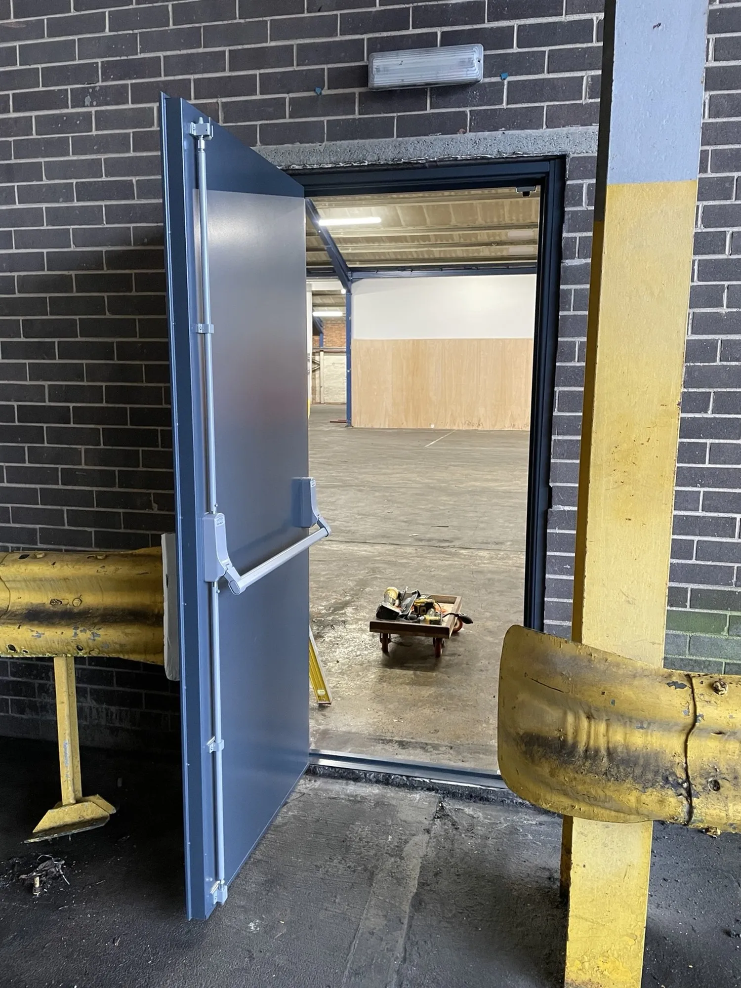 New steel exit door hung and operating, swung open to show the clear escape opening into the unit