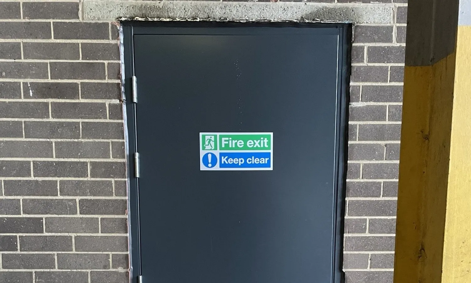 Completed steel fire exit door fitted by Coulsy Fire Doors on a commercial unit, with a green 'Fire exit / Keep clear' sign